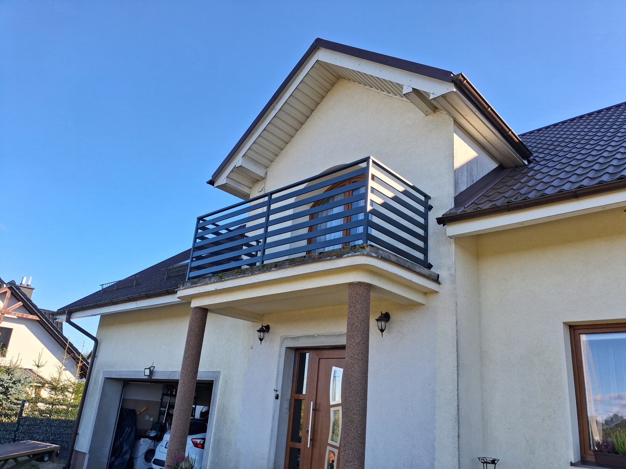 Dom z balkonem zabezpieczonym nowoczesną, poziomą konstrukcją. Ujęcie z dołu, podkreślające architekturę budynku i minimalistyczny design.