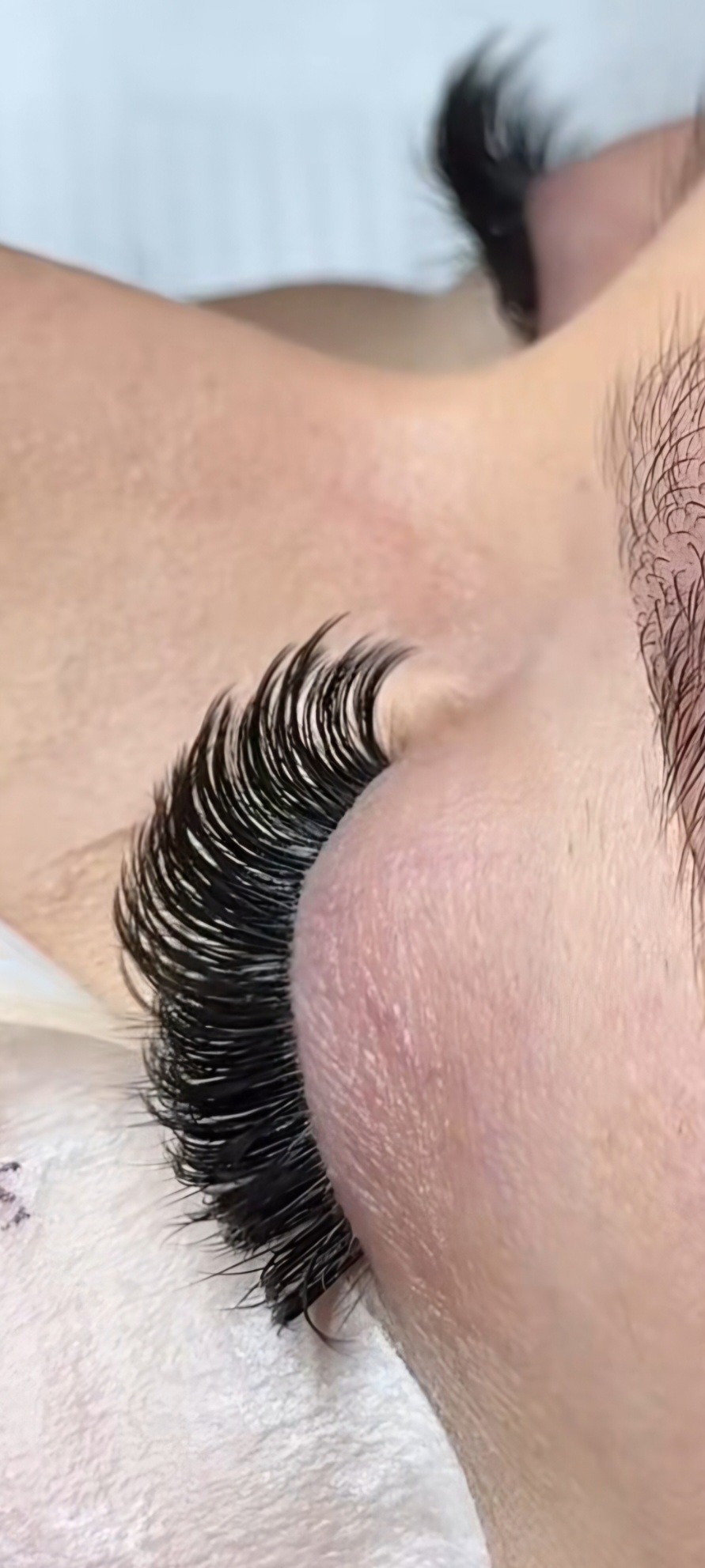 Zbliżenie na oko z wyraźnie przedłużonymi, gęstymi rzęsami w odcieniu głębokiej czerni. Widoczny fragment brwi i skóry.