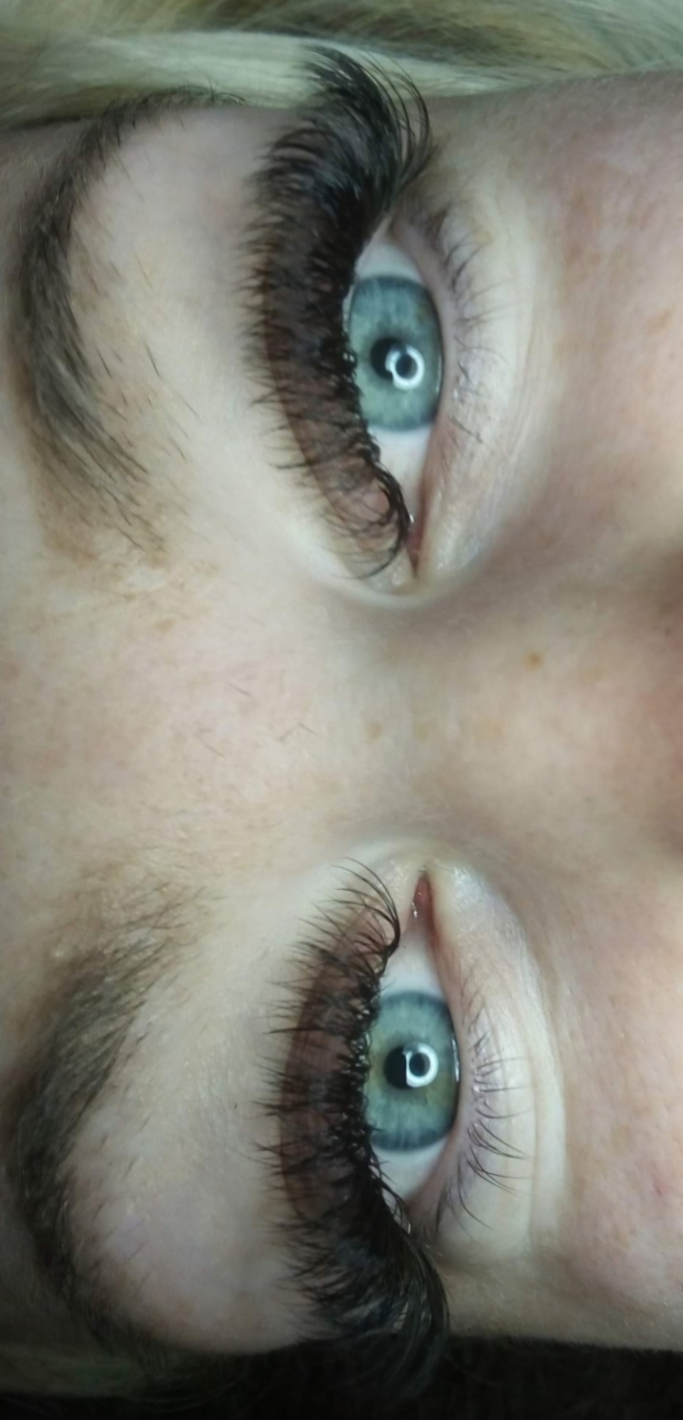 Zbliżenie na niebieskie oczy z gęstymi, ciemnymi rzęsami po zabiegu przedłużania. Widoczna skóra i delikatny makijaż. Oświetlenie studyjne.