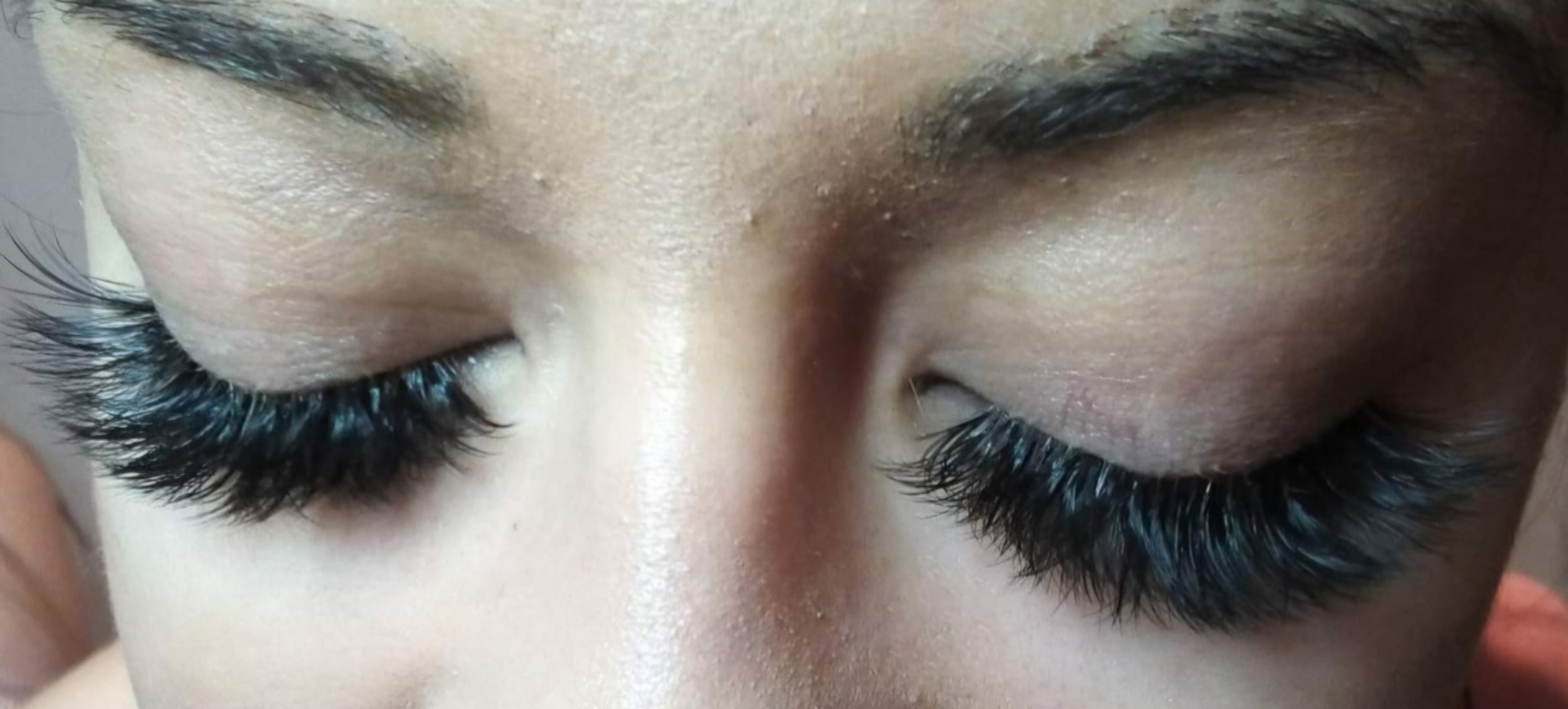 Zbliżenie na zamknięte oczy z dramatycznie długimi, czarnymi sztucznymi rzęsami, podkreślającymi wyrazistość spojrzenia. Delikatny makijaż brwi.