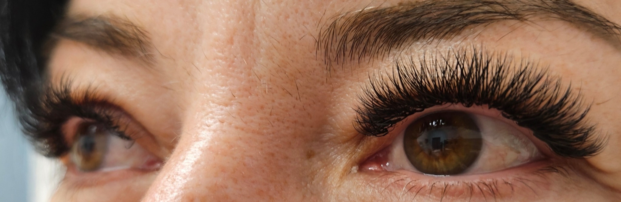 Zbliżenie na oko z wyraźnie przedłużonymi, gęstymi rzęsami. Widoczny brązowy kolor tęczówki i precyzyjna aplikacja sztucznych rzęs, podkreślająca naturalne piękno.