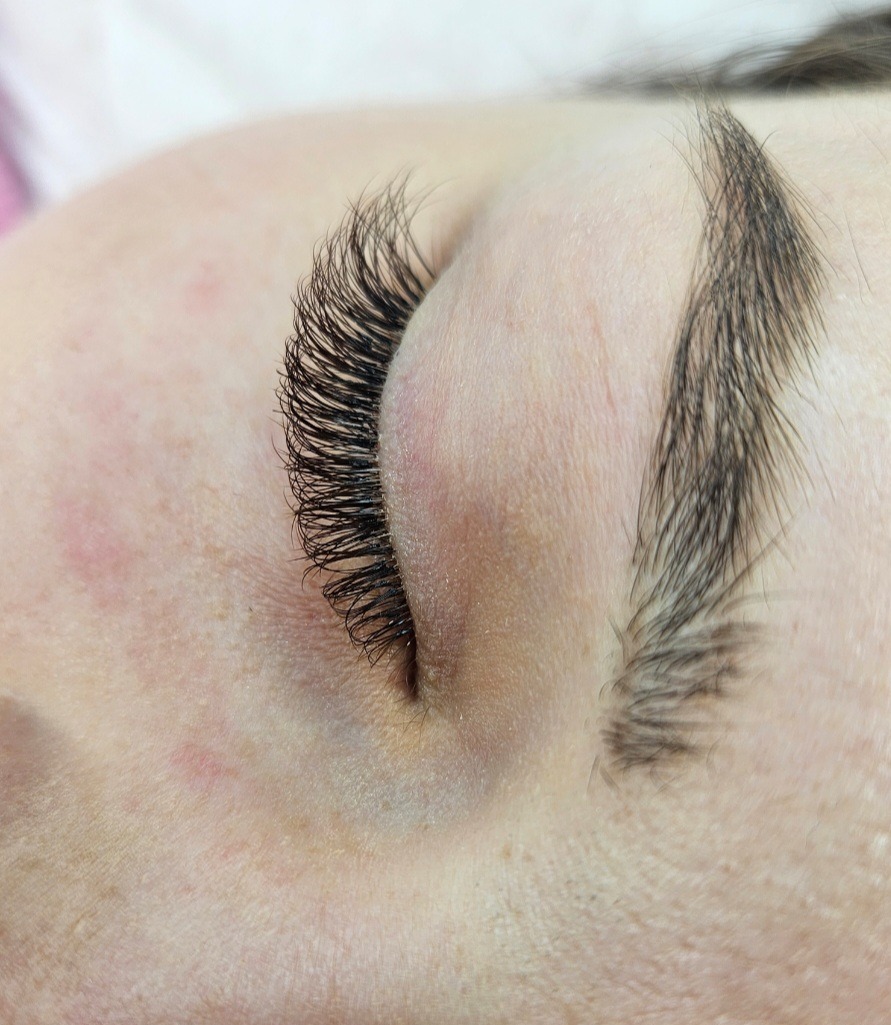 Zbliżenie na oko po zabiegu przedłużania rzęs metodą objętościową. Widoczne gęste, czarne rzęsy i naturalne brwi. Delikatny makijaż podkreśla efekt.