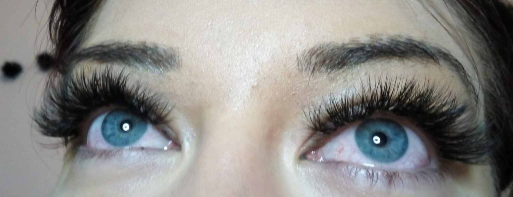 Zbliżenie na niebieskie oczy z wyraźnie przedłużonymi, gęstymi rzęsami. Widoczne delikatne zaczerwienienie w kącikach oczu. Makijaż akcentuje spojrzenie.