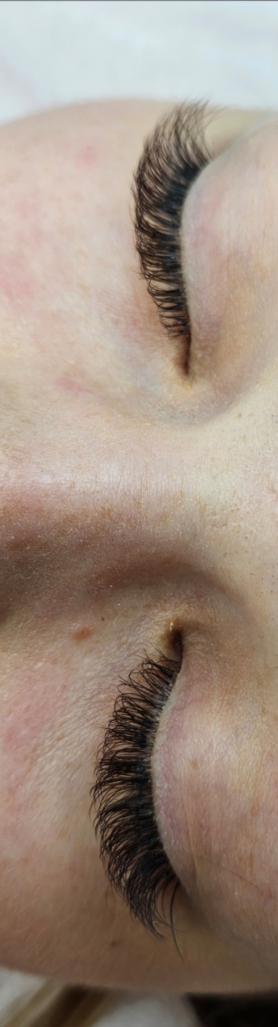 Zbliżenie na oko po zabiegu przedłużania rzęs. Widoczne gęste, czarne rzęsy. Skóra jasna, z widocznymi drobnymi niedoskonałościami.