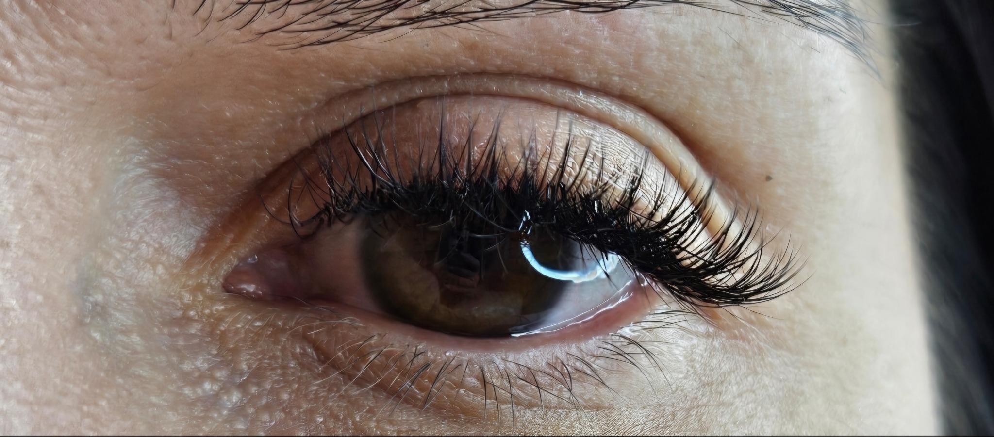 Zbliżenie na oko z wyraźnie wydłużonymi, czarnymi rzęsami. Widoczny delikatny blask w źrenicy i szczegółowa tekstura skóry wokół oka. Makro.