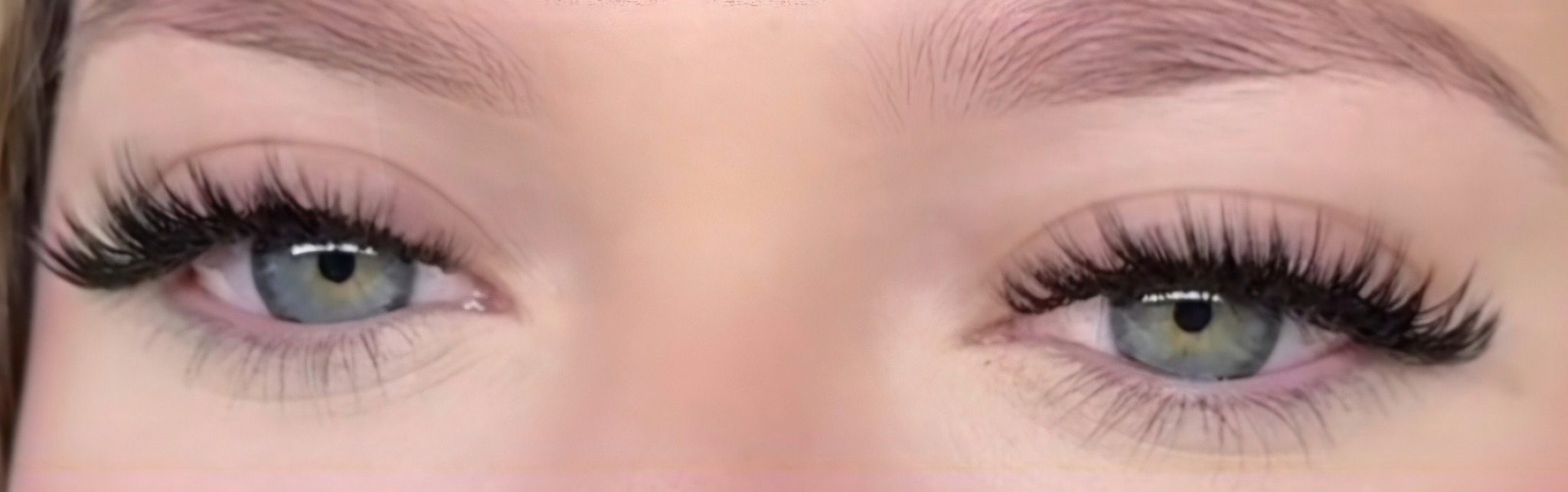 Zbliżenie na parę niebiesko-zielonych oczu z wyraźnie wydłużonymi, czarnymi rzęsami, podkreślającymi efekt liftingu i zagęszczenia w gabinecie kosmetycznym.