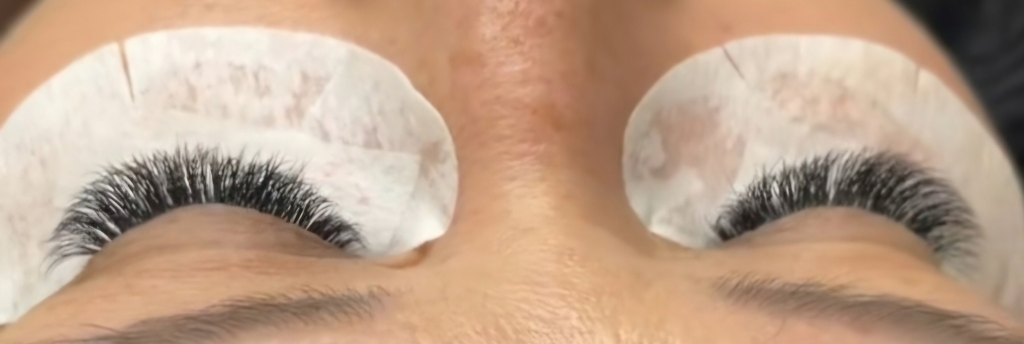 Zbliżenie na oczy klientki po zabiegu przedłużania rzęs metodą objętościową. Widoczne podkładki ochronne pod oczami i gęste, czarne rzęsy.