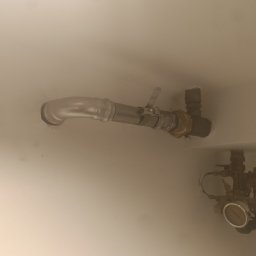 Bartosz Jaworski Usługi Ogólnobudowlane - Metalowa rura instalacyjna, z zaworem i złączkami, zamontowana na jasnej ścianie. Widoczny manometr i fragment instalacji w tle.