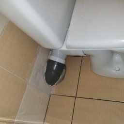 Bartosz Jaworski Usługi Ogólnobudowlane - Ukończone podłączenie odpływu toalety z użyciem elastycznej rury, z widocznym uszczelnieniem przy podłodze z płytek. Detal z bliska, po montażu.