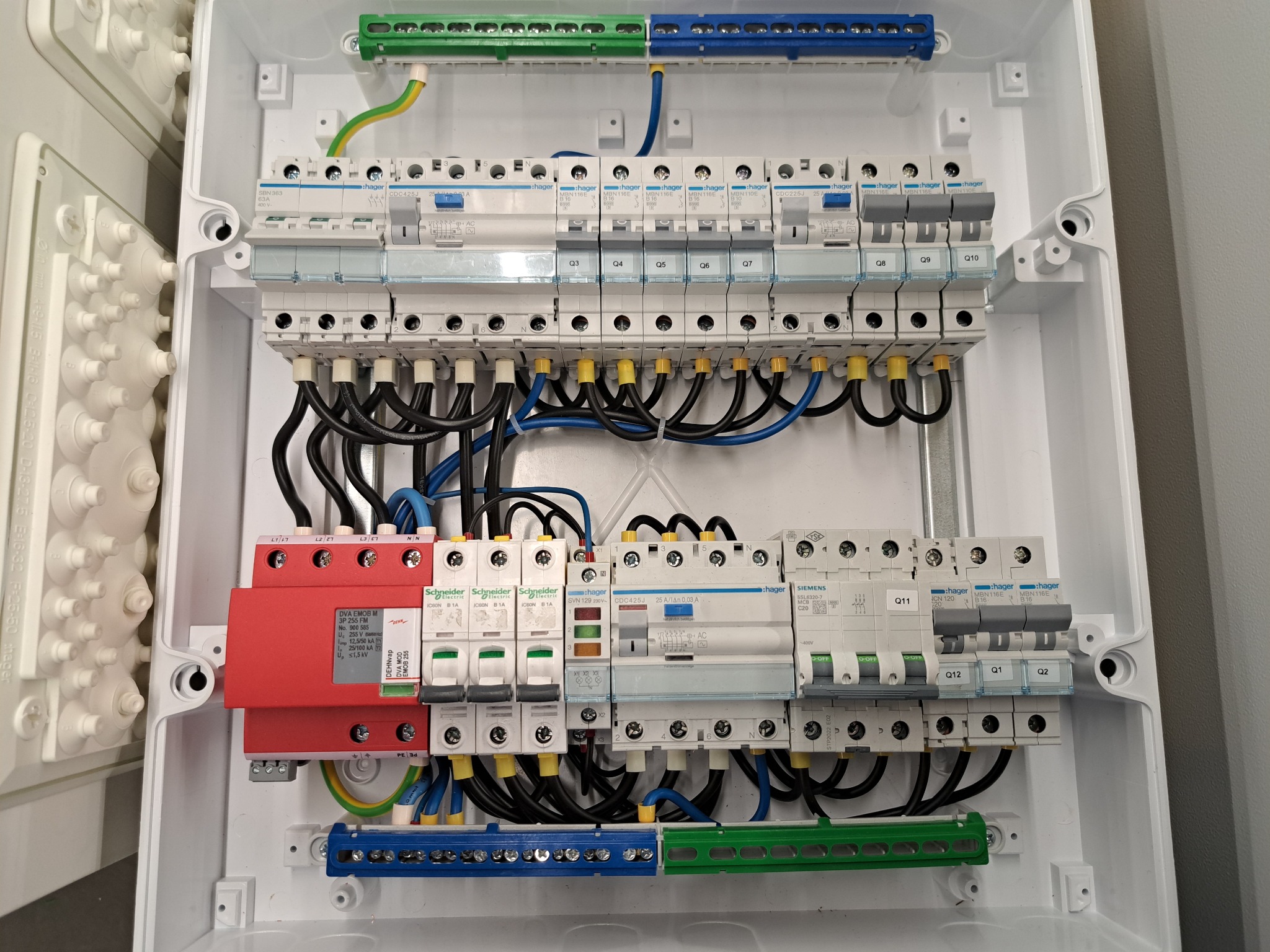 Rozdzielnica elektryczna w białej obudowie, z widocznymi bezpiecznikami, przewodami i elementami montażowymi. Starannie wykonana instalacja.