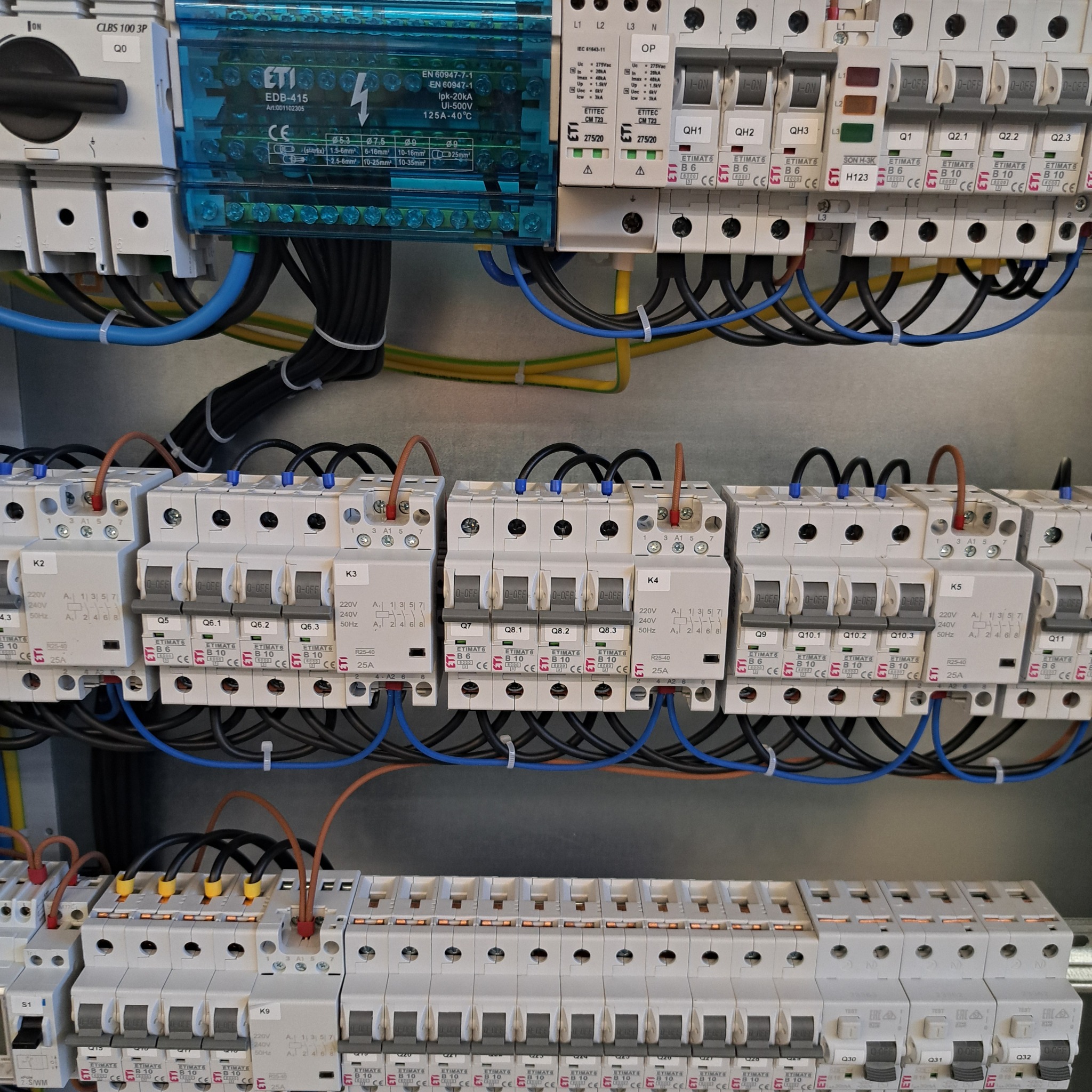 Rozdzielnica elektryczna z bezpiecznikami i okablowaniem, widok z bliska. Elementy instalacji elektrycznej w skrzynce rozdzielczej, kable uporządkowane.