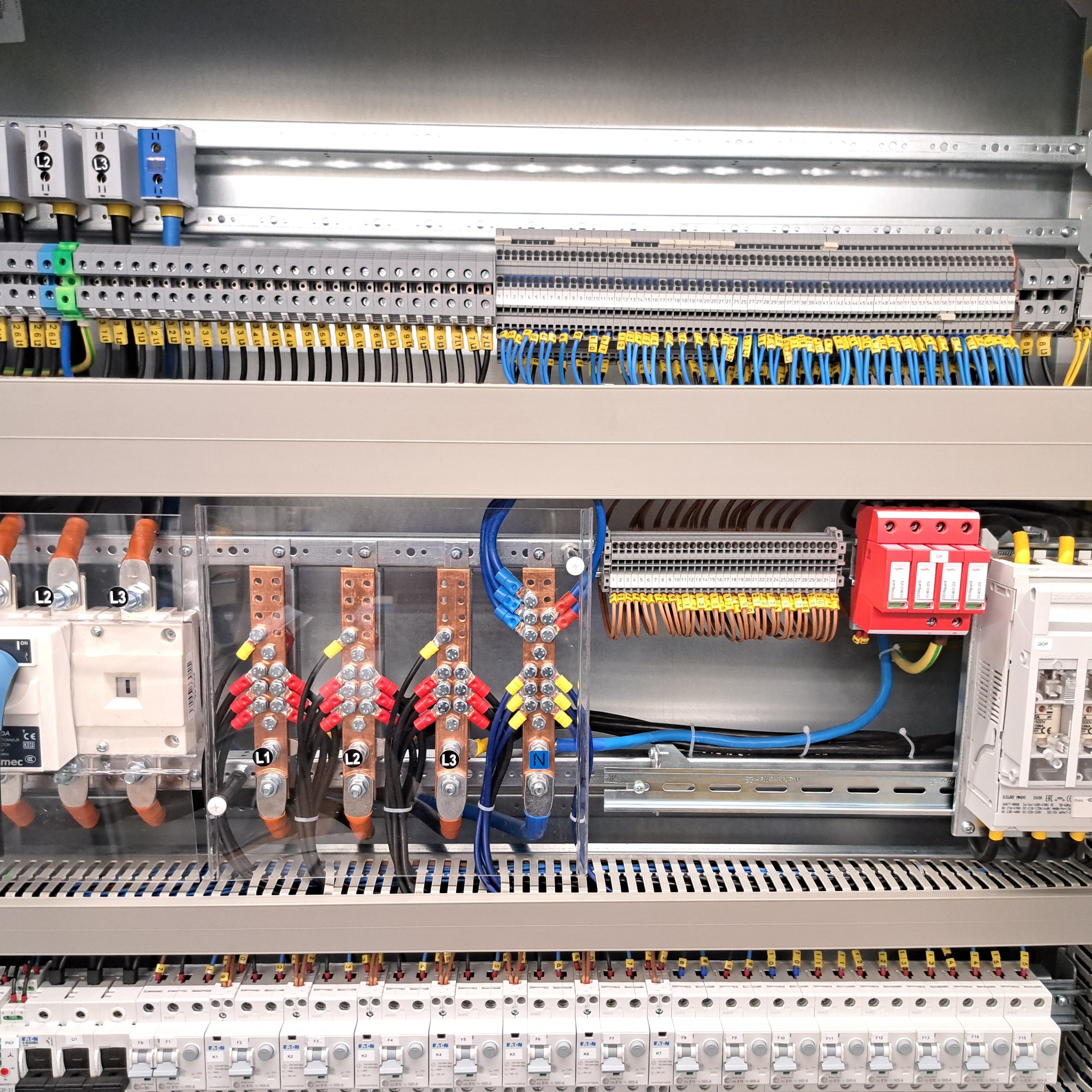 Rozdzielnica elektryczna z precyzyjnie ułożonymi kablami i zabezpieczeniami, widoczne oznaczenia L1, L2, L3, N. Starannie wykonana instalacja w skrzynce rozdzielczej.