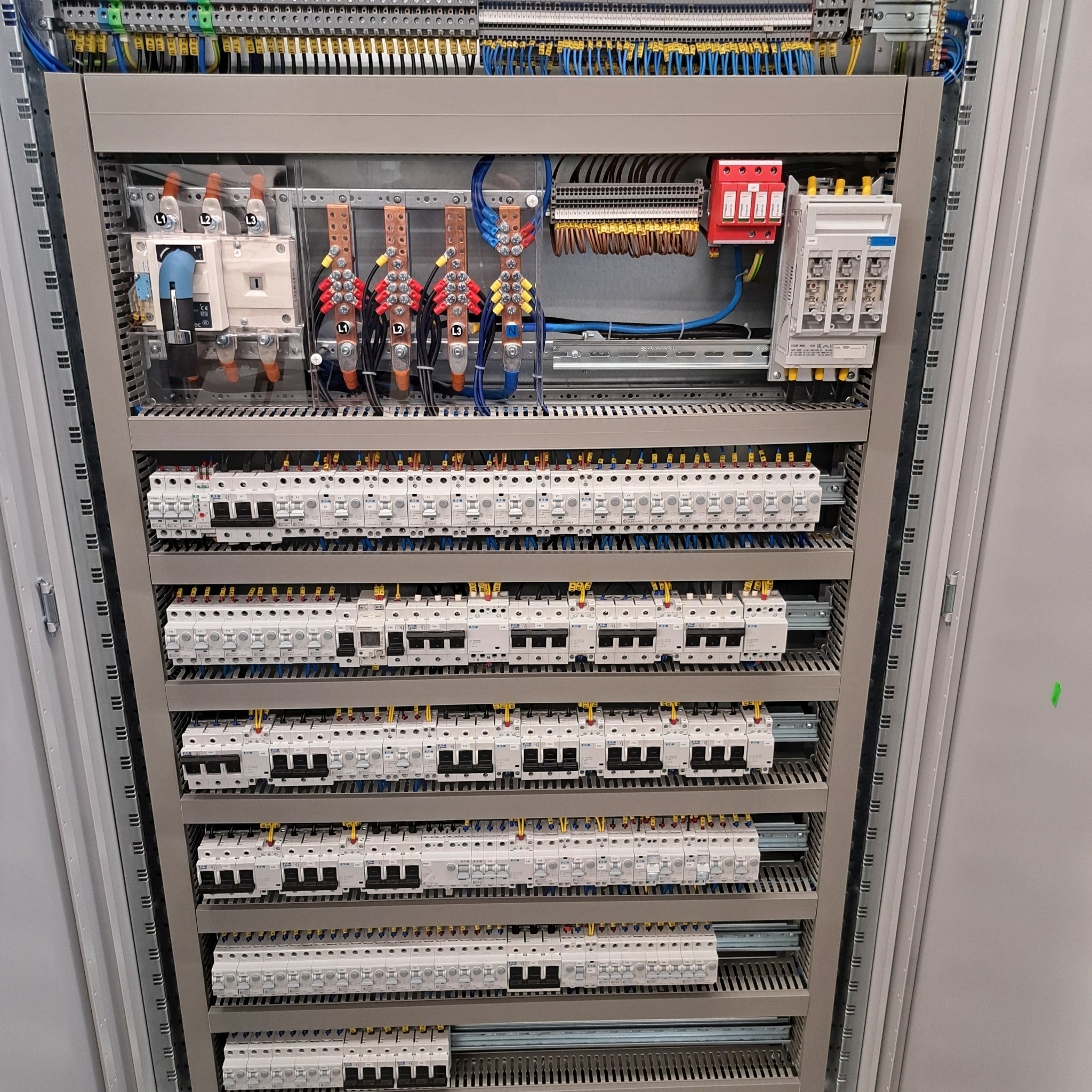 Rozdzielnica elektryczna z licznymi zabezpieczeniami, bezpiecznikami i przewodami. Widoczne elementy instalacji elektrycznej w szafie sterowniczej.