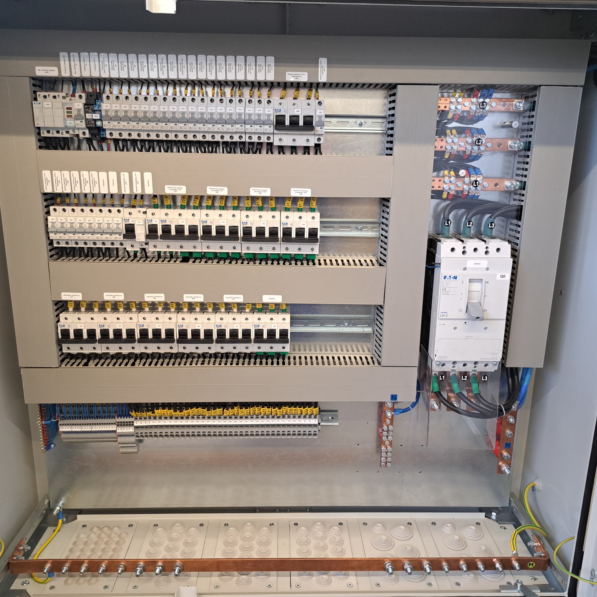 Rozdzielnica elektryczna z bezpiecznikami, okablowaniem i listwami zaciskowymi. Widoczne komponenty Eaton. Precyzyjny montaż w szarej obudowie.