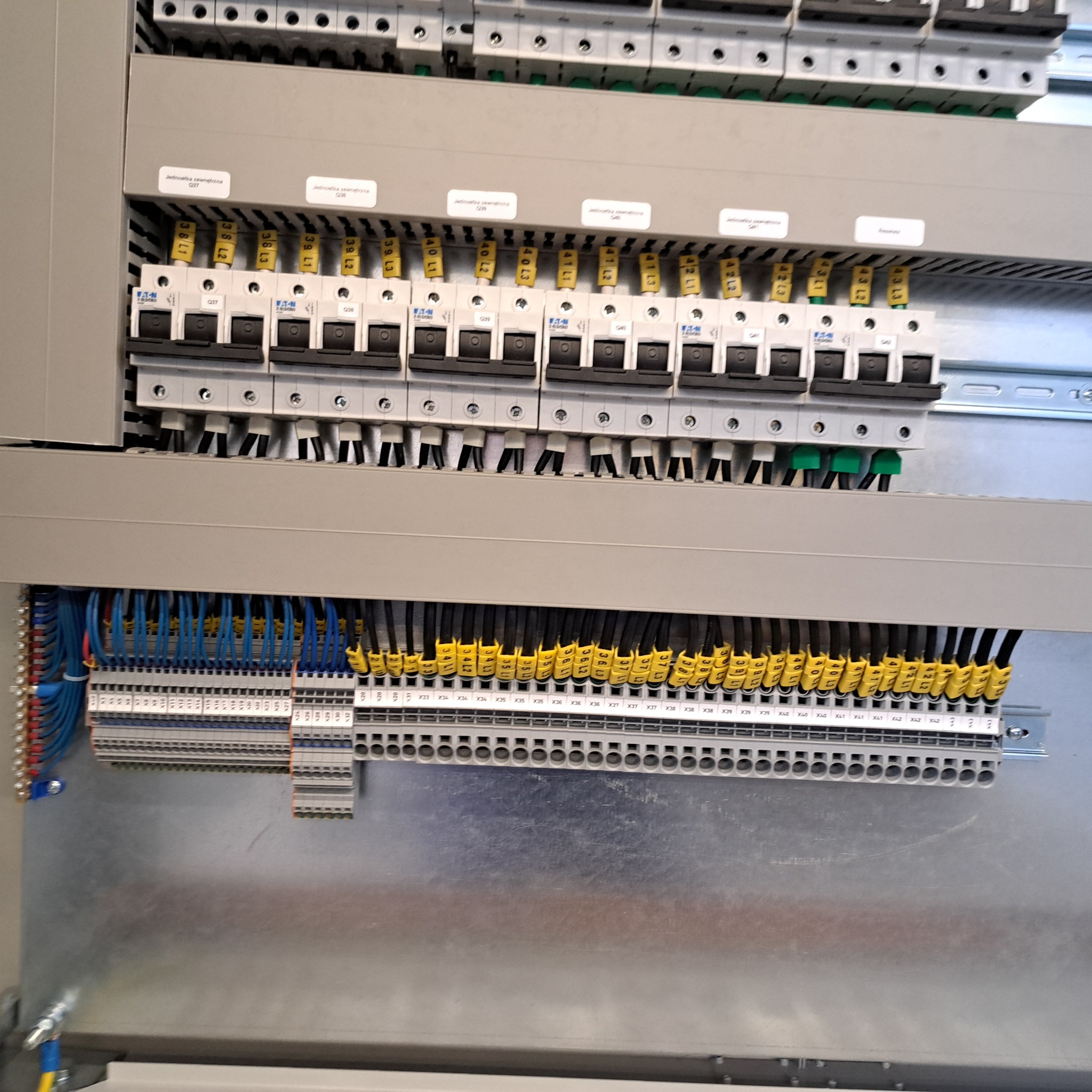 Szczegółowe ujęcie rozdzielnicy elektrycznej z bezpiecznikami, okablowaniem oznaczonym żółtymi numerowanymi tulejkami i listwami zaciskowymi.