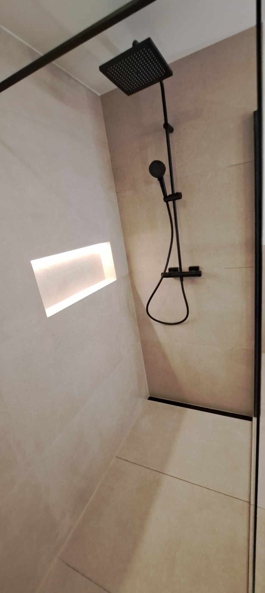 Minimalistyczna kabina prysznicowa z beżowymi płytkami, czarną armaturą i wnęką z podświetleniem LED. Nowoczesny design, eleganckie wykończenie.