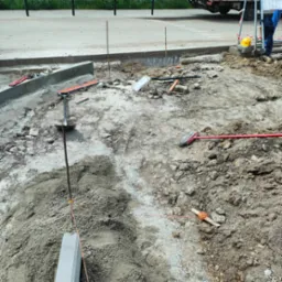 Przygotowanie terenu pod chodnik: widoczne narzędzia (szpadel, poziomica), obrzeża, wytyczone linie. Etap prac ziemnych przed ułożeniem nawierzchni.