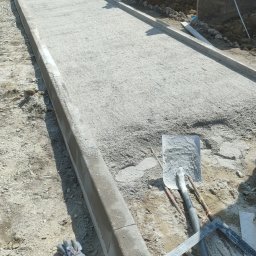 PRIME ROAD WIESŁAW BŁASIK - Przygotowany podkład z kruszywa pod chodnik z obrzeżami, widoczne narzędzia i maszyna do cięcia. Etap prac przed ułożeniem nawierzchni.
