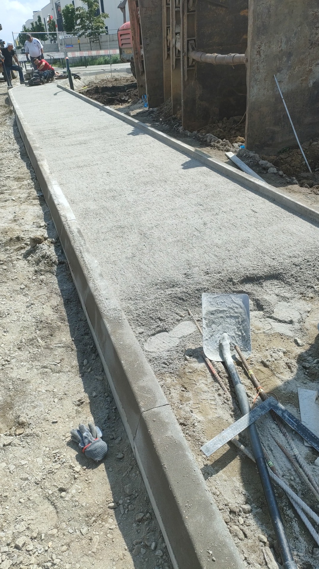 Przygotowany podkład z kruszywa pod chodnik z obrzeżami, widoczne narzędzia i maszyna do cięcia. Etap prac przed ułożeniem nawierzchni.