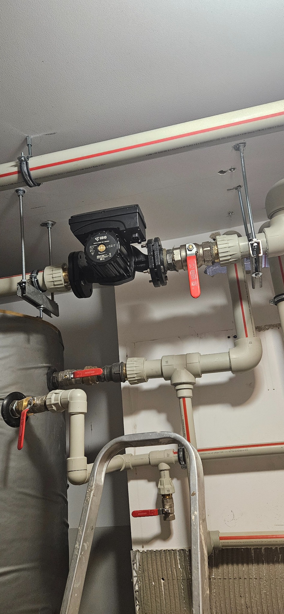 Zamontowana pompa obiegowa IBO Nova Max 50-120/250 z rurami, zaworami i zbiornikiem w instalacji grzewczej. Widoczna drabina.