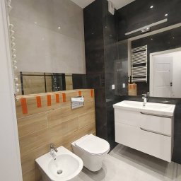 Patrykdys - Nowoczesna łazienka z wiszącą toaletą, bidetem i umywalką z szafką. Na ścianach płytki imitujące drewno i ciemny kamień. Lustro na ścianie powiększa przestrzeń.