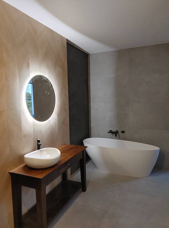 Nowoczesna łazienka w Dzierzkowicach z wolnostojącą wanną, umywalką na drewnianym blacie i okrągłym lustrem z podświetleniem LED.