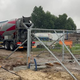 CENTRUM REALIZACJI PROSTA SPÓŁKA AKCYJNA - Betoniarka w trakcie wylewania fundamentów pod ogrodzenie na placu budowy, widoczne narzędzia i tymczasowe zabezpieczenia.