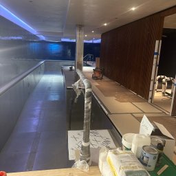 Perfection pro design ING - Wnętrze w trakcie wykończenia basenu z niebieskim oświetleniem, widoczne materiały budowlane, narzędzia i pracownicy w kombinezonach ochronnych.