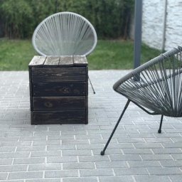 Czysty Ejber - Szara kostka brukowa z drewnianą skrzynią i krzesłami w stylu Acapulco. Trawa i bambus w tle. Widok na czystą, zadbaną przestrzeń.