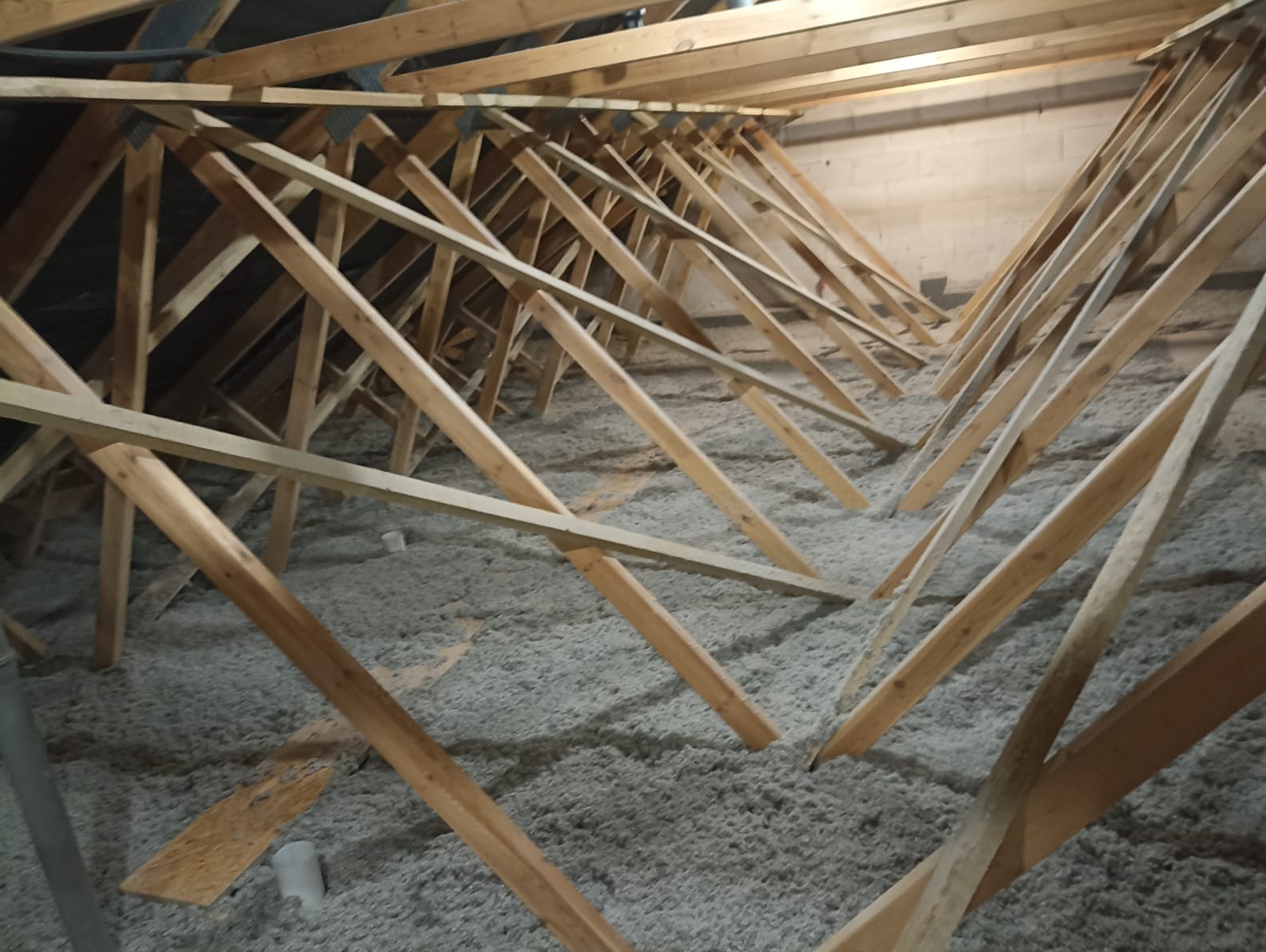 Poddasze z widoczną konstrukcją drewnianą i szarą izolacją z wełny mineralnej. Ukończony etap prac, widok z dołu.