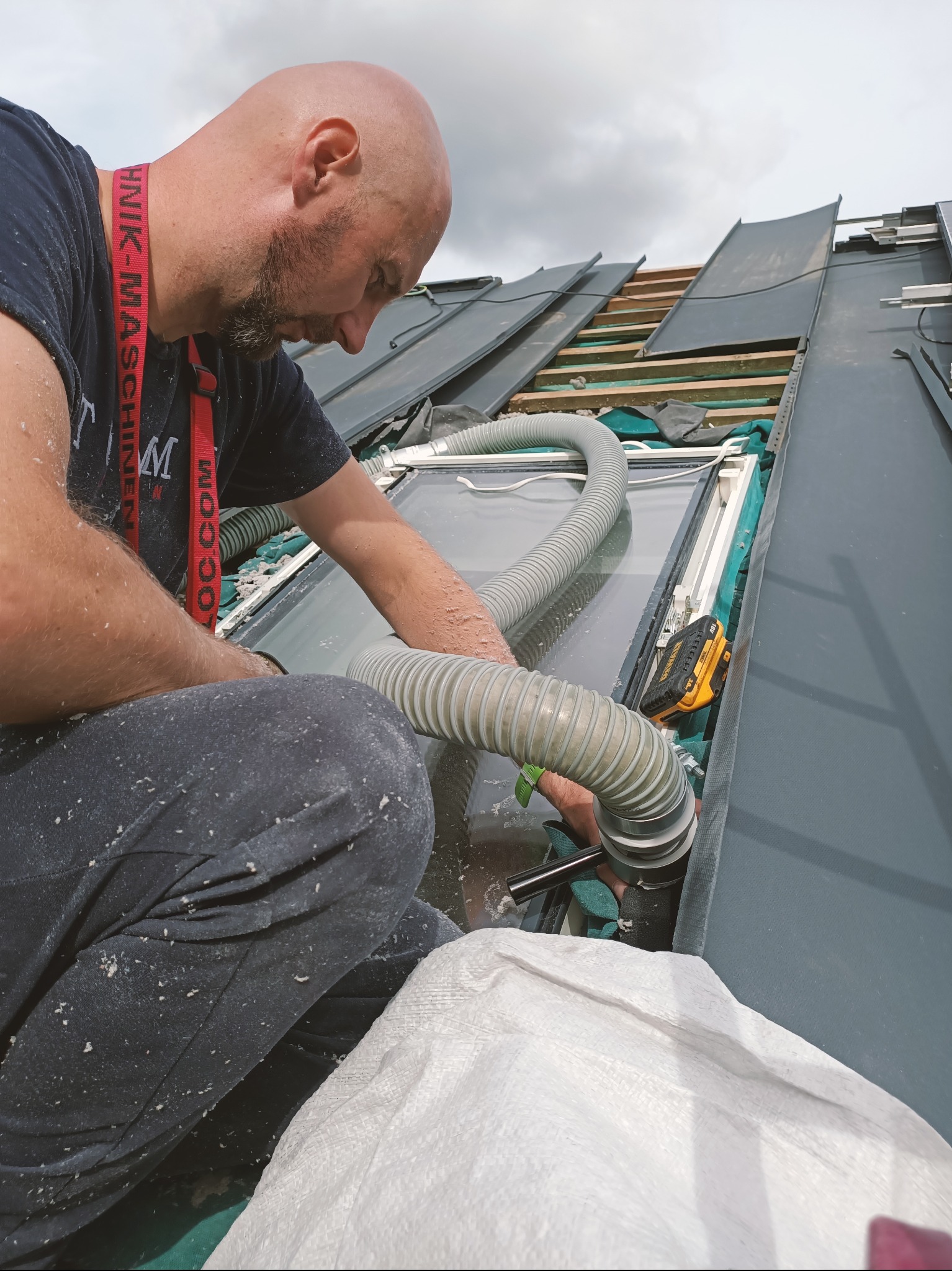 Pracownik w trakcie wdmuchiwania izolacji do przestrzeni okna dachowego na poddaszu. Widoczny wąż, narzędzia i częściowo odsłonięta konstrukcja dachu.