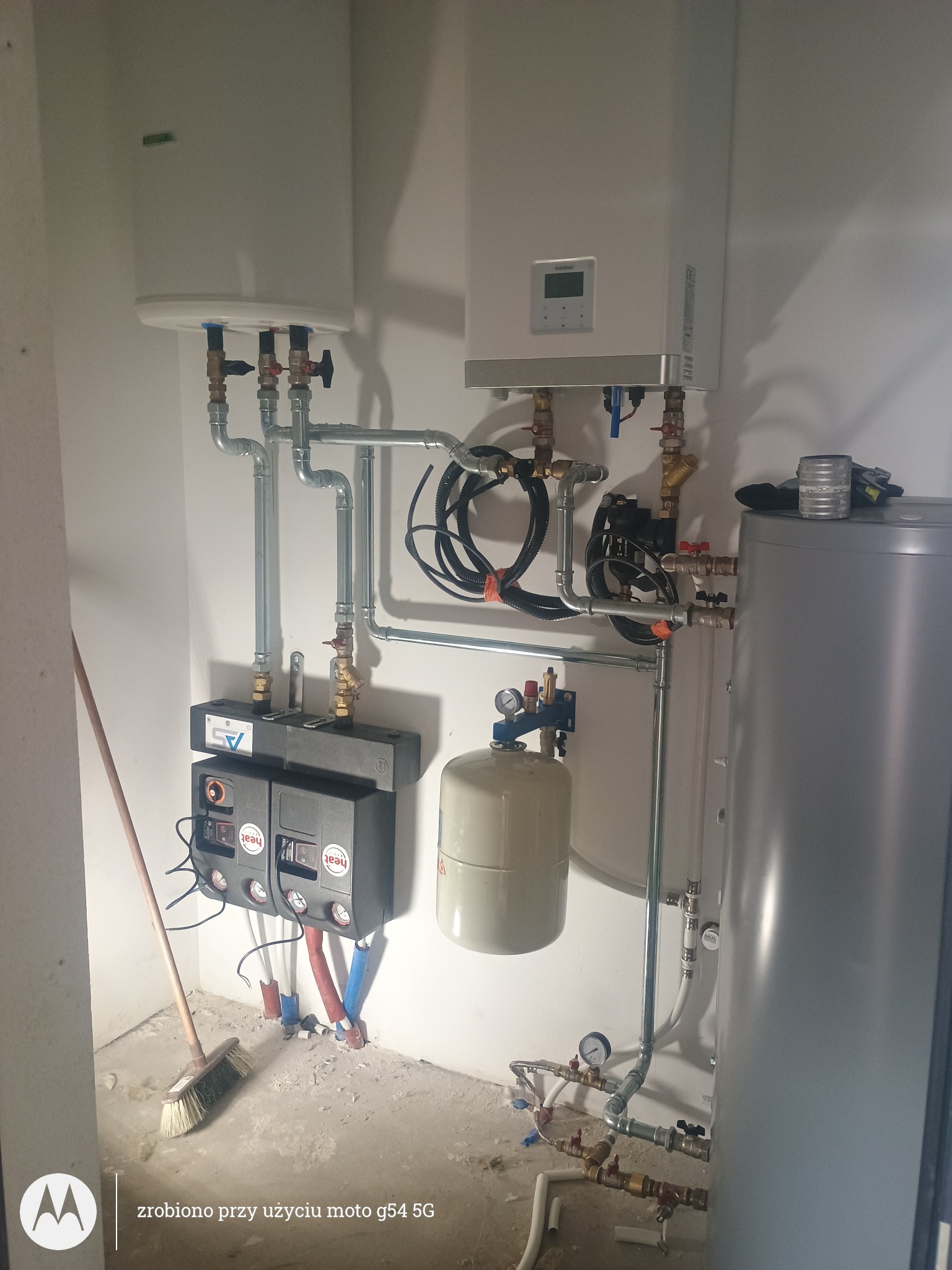 Złożona instalacja grzewcza z piecem i zbiornikiem w Policzna. Rury, zawory i czujniki tworzą system. Widoczny bałagan po montażu, czekający na posprzątanie.
