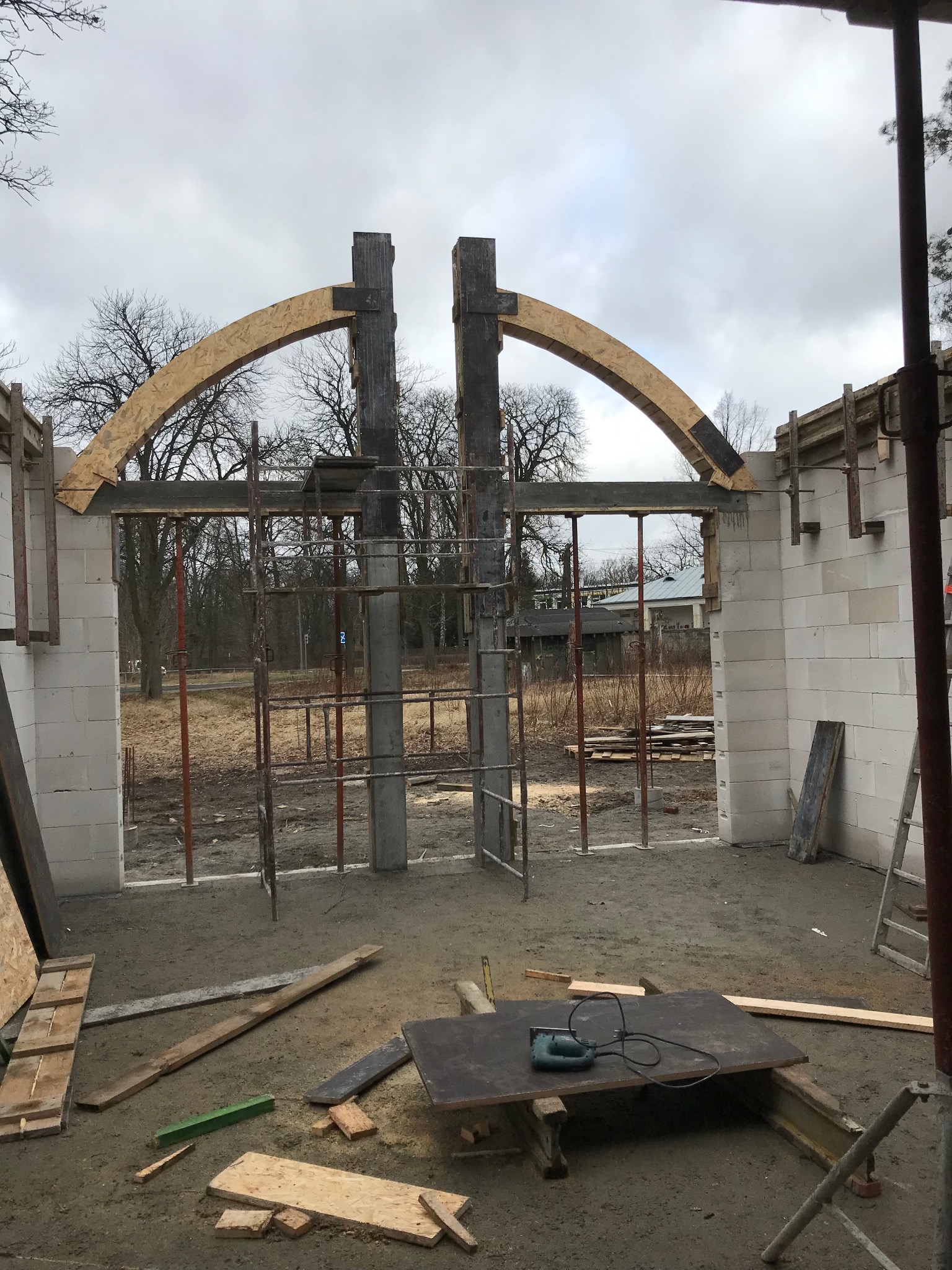 Wznoszenie łuku nad otworem w ścianie z betonu komórkowego. Konstrukcja wsparta na rusztowaniach. Na pierwszym planie narzędzia i deski.