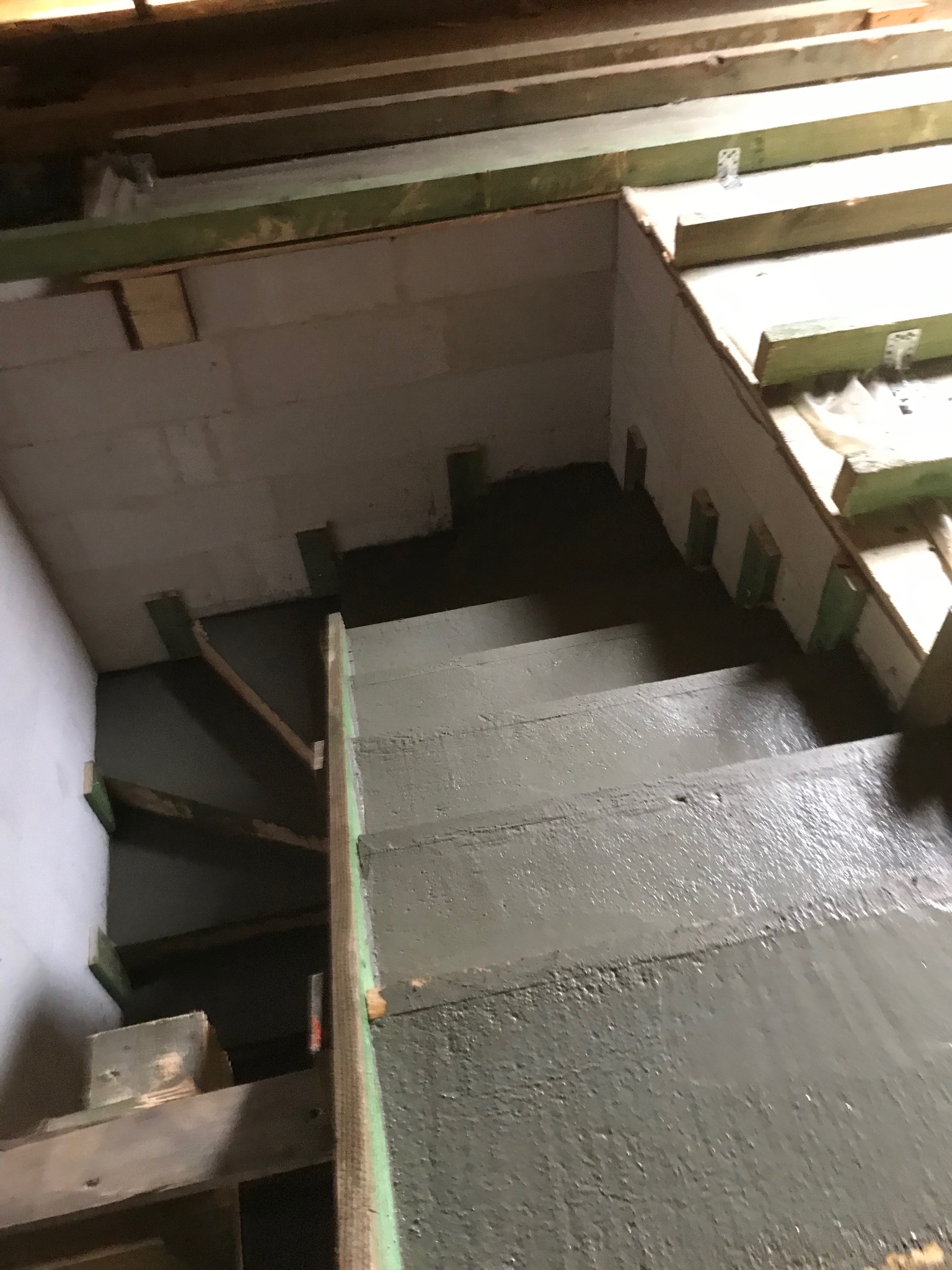 Wylane schody betonowe w surowym stanie, widoczne szalunki i bloczki betonowe. Ujęcie z góry, surowe oświetlenie wnętrza. Etap budowy.