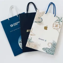 Trzy papierowe torby reklamowe z różnymi nadrukami, prezentujące realizacje z Gdańska. Torby w kolorach: granatowy, czarny i biały z elementami graficznymi.