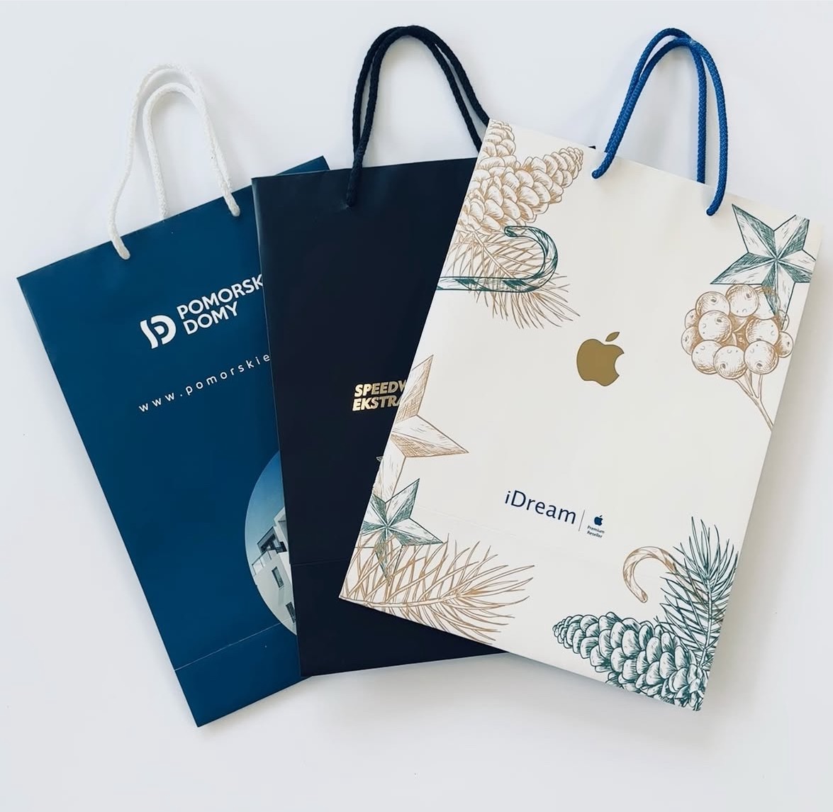Trzy papierowe torby reklamowe z różnymi nadrukami, prezentujące realizacje z Gdańska. Torby w kolorach: granatowy, czarny i biały z elementami graficznymi.