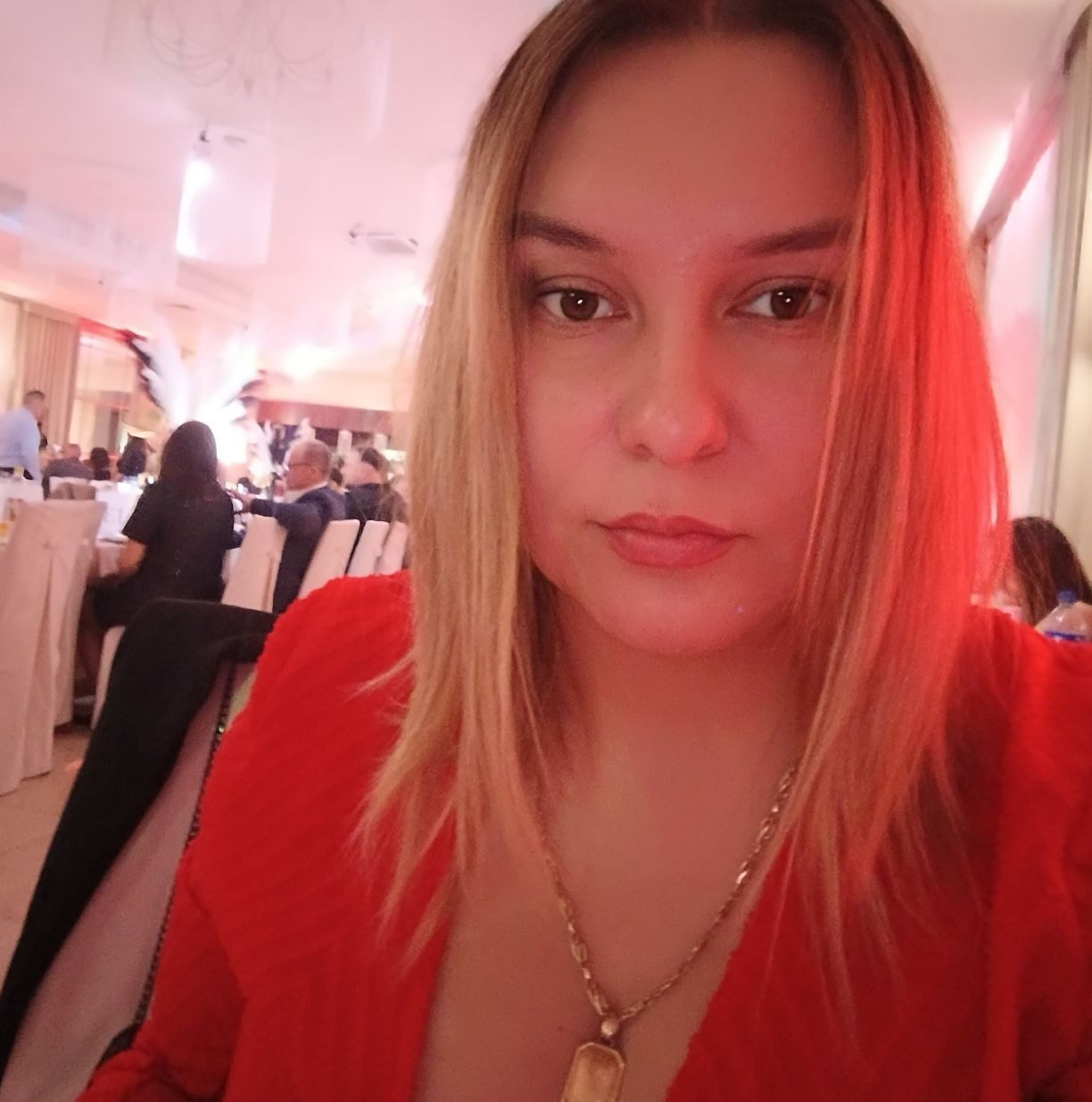 Portret kobiety w czerwonej bluzce na tle sali bankietowej, możliwe zdjęcie z imprezy firmowej, z widocznym oświetleniem i uczestnikami w tle.