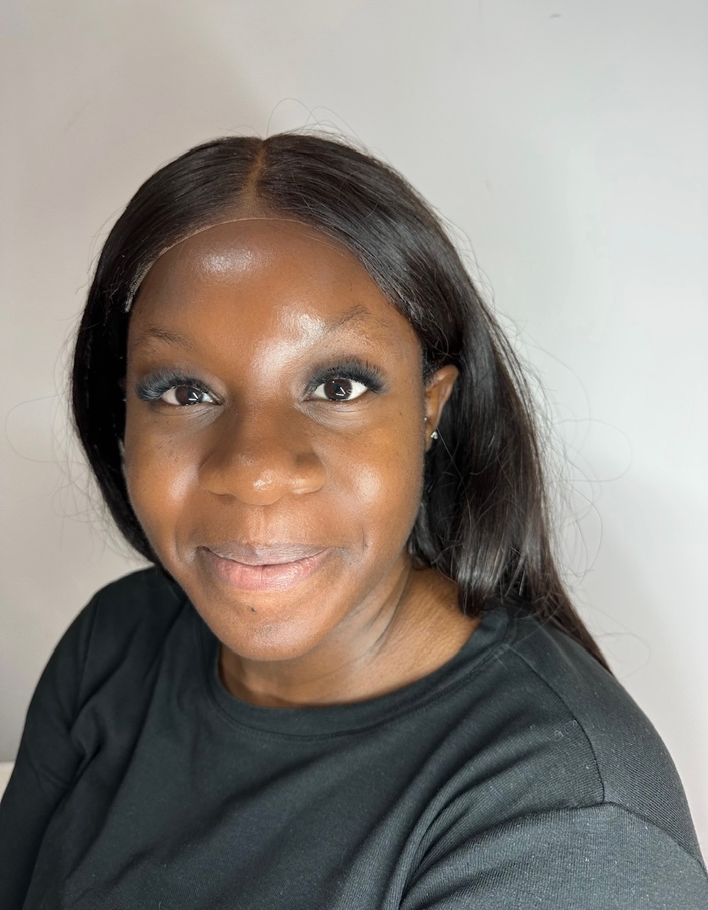 Portret kobiety z delikatnym makijażem oczu, gładkimi włosami i subtelnym uśmiechem na jasnym tle. Widoczne świeże spojrzenie i zadbana cera.