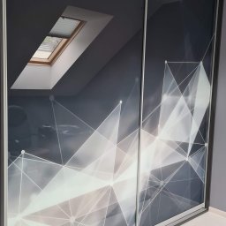 Penele szklane Glassing - Dwudrzwiowa szafa wnękowa z przesuwnymi drzwiami, na których widnieje graficzny wzór białych linii na szarym tle. W tle okno dachowe.