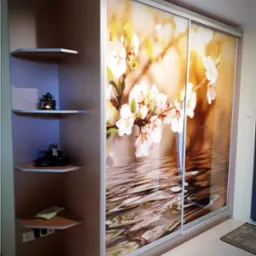 Dwudrzwiowa szafa wnękowa z grafiką kwitnącej wiśni na tle wody, widoczna z boku, z narożnymi półkami po lewej stronie. Jasne wnętrze, dywanik w rogu.