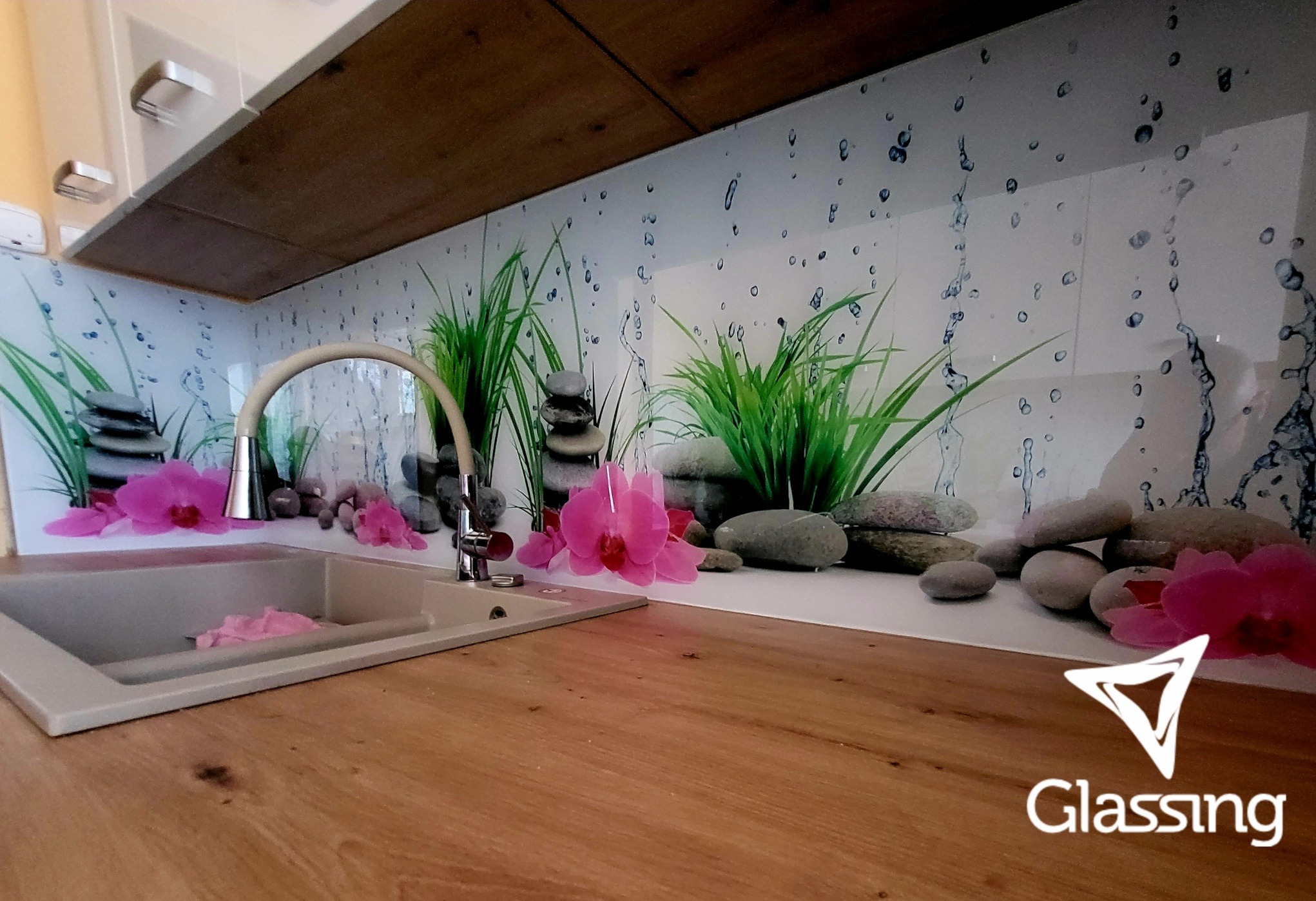 Szklany panel dekoracyjny nad blatem kuchennym z motywem zen: kamienie, orchidee i krople wody, nowoczesna aranżacja z drewnianym blatem.