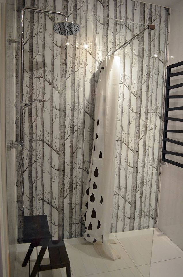 Nowoczesna łazienka z kabiną prysznicową, deszczownicą i zasłoną w krople na tle tapety z motywem brzozowego lasu. Widoczny czarny grzejnik.