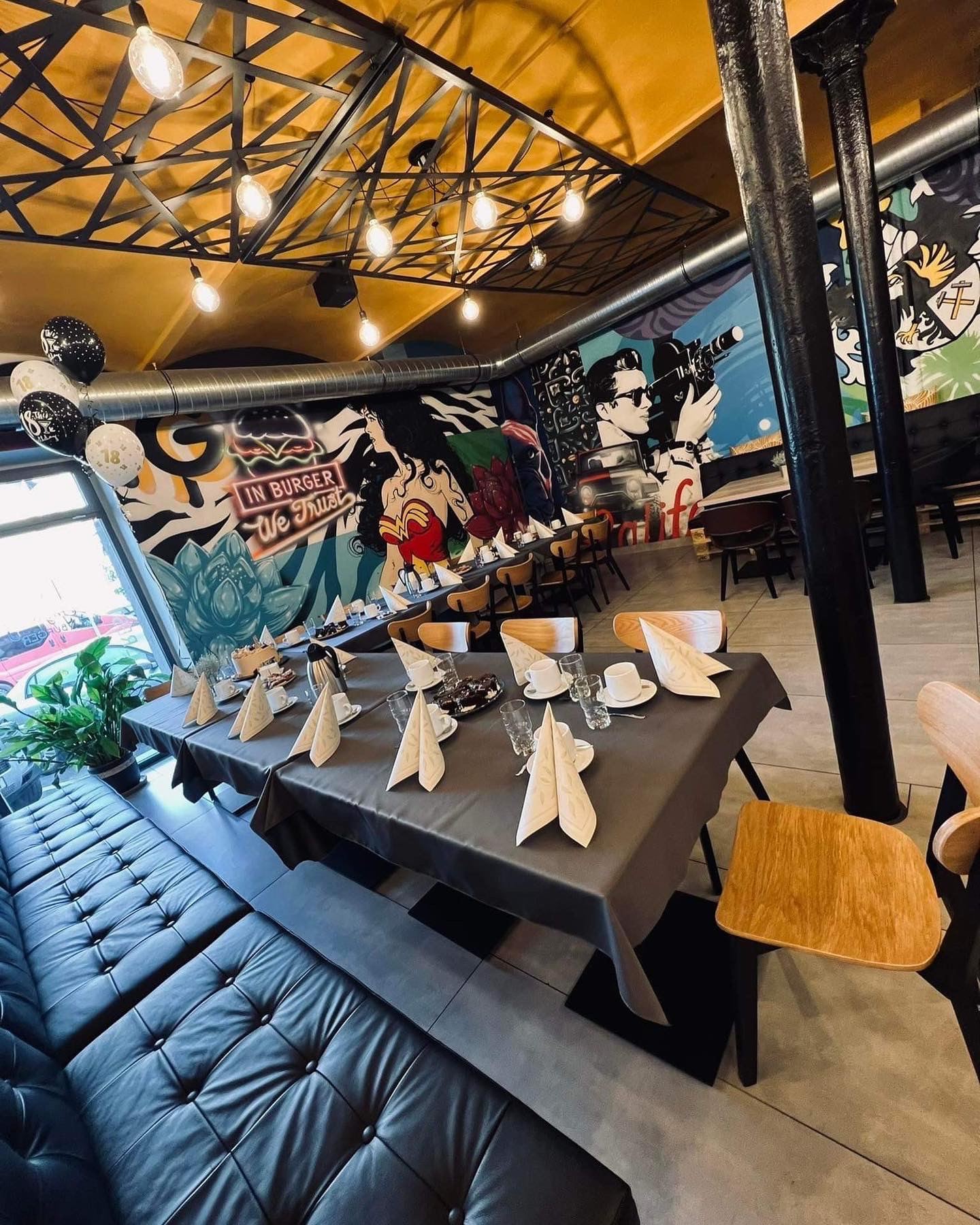 Przygotowany stół z dekoracjami i tortem w restauracji z muralami. Ustawienia stołowe, balony z cyfrą 18. Dekoracja na osiemnastkę w lokalu.