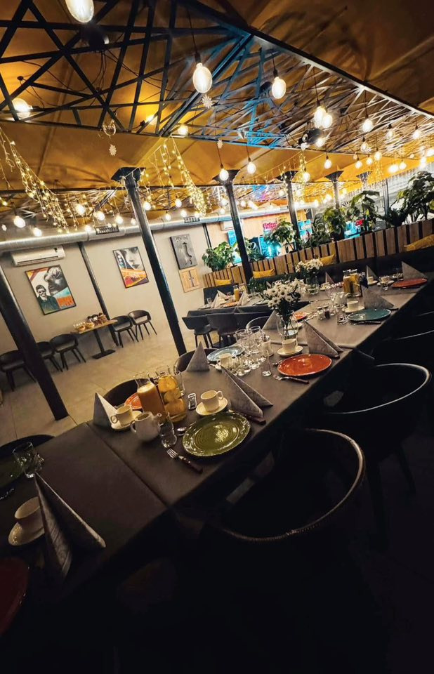 Uroczysty stół z zastawą, dekoracjami i napojami w przestronnej sali z oświetleniem girlandami, gotowy na przyjęcie gości podczas eventu.