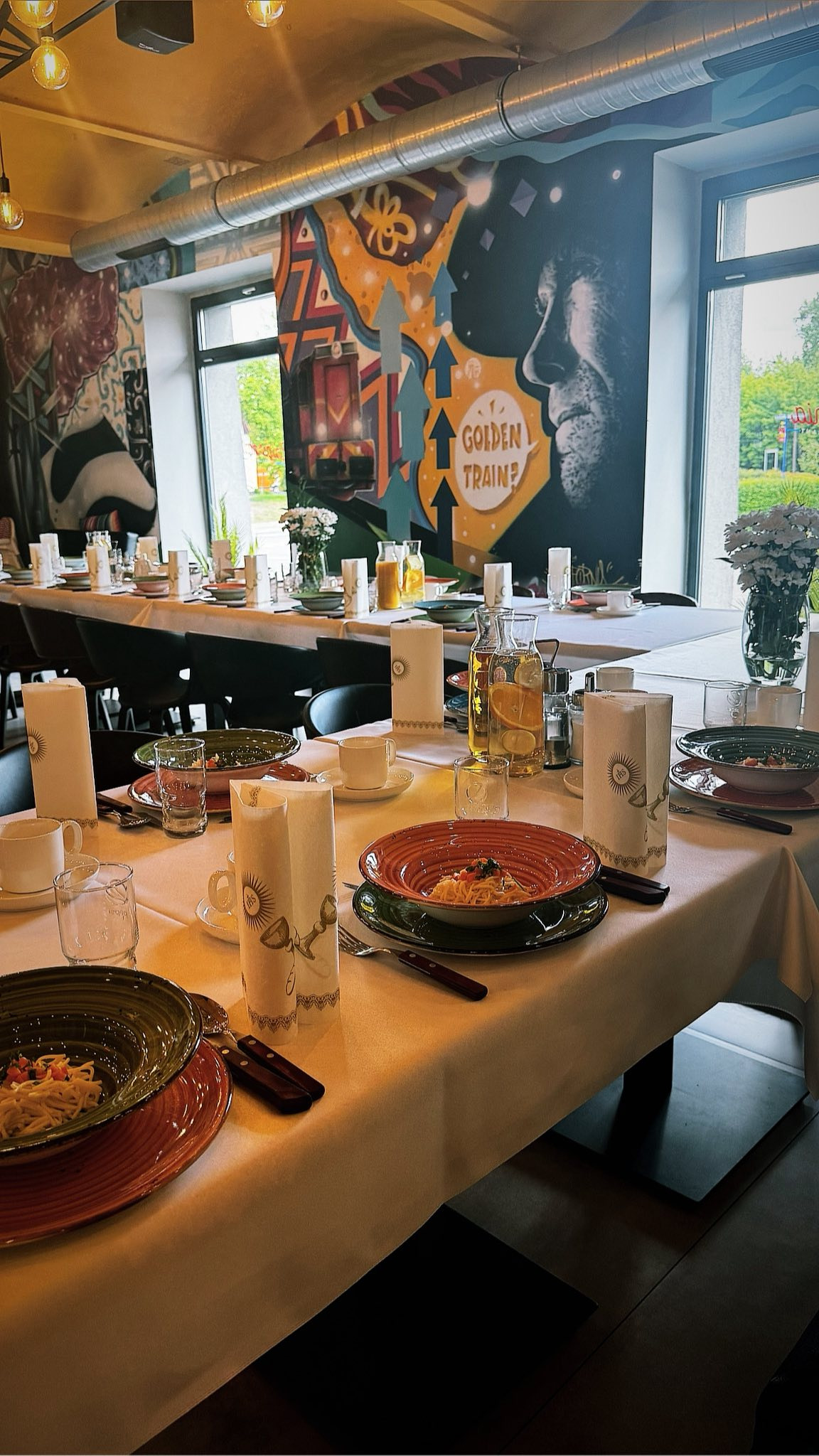 Uroczysty stół z nakryciami, talerzami z daniem, szklankami i dekoracjami kwiatowymi w restauracji z muralem. Przygotowania do eventu.