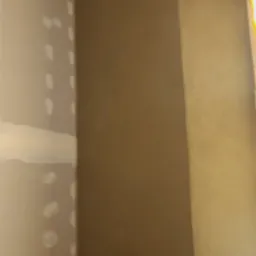 Ściana po nałożeniu gładzi w odcieniach beżu, widoczne fragmenty zaszpachlowanej ściany gipsowej w rogu pomieszczenia, przygotowanie do malowania.