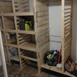 Konstrukcja garderoby z surowego drewna, z półkami i drążkiem, w trakcie montażu. Widoczne narzędzia i torba narzędziowa. Prosta forma, naturalne materiały.