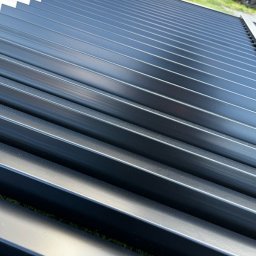 FusionWW - Czarne, metalowe lamele ogrodzeniowe ułożone równolegle na trawie, widok z góry pod kątem. Elementy przygotowane do montażu.