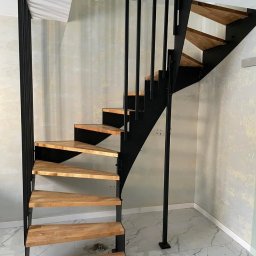 FusionWW - Nowoczesne schody metalowe z drewnianymi stopniami, czarna konstrukcja, jasne tło. Widok z dołu ukazuje solidne wykonanie i minimalistyczny design.