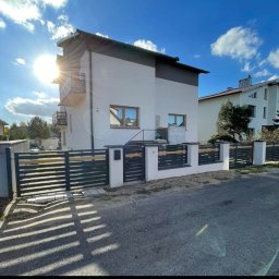 FusionWW - Nowoczesne ogrodzenie panelowe z poziomymi, ciemnymi przęsłami i jasnymi słupkami na tle dwukondygnacyjnego domu w słoneczny dzień. Brama przesuwna częściowo otwarta.